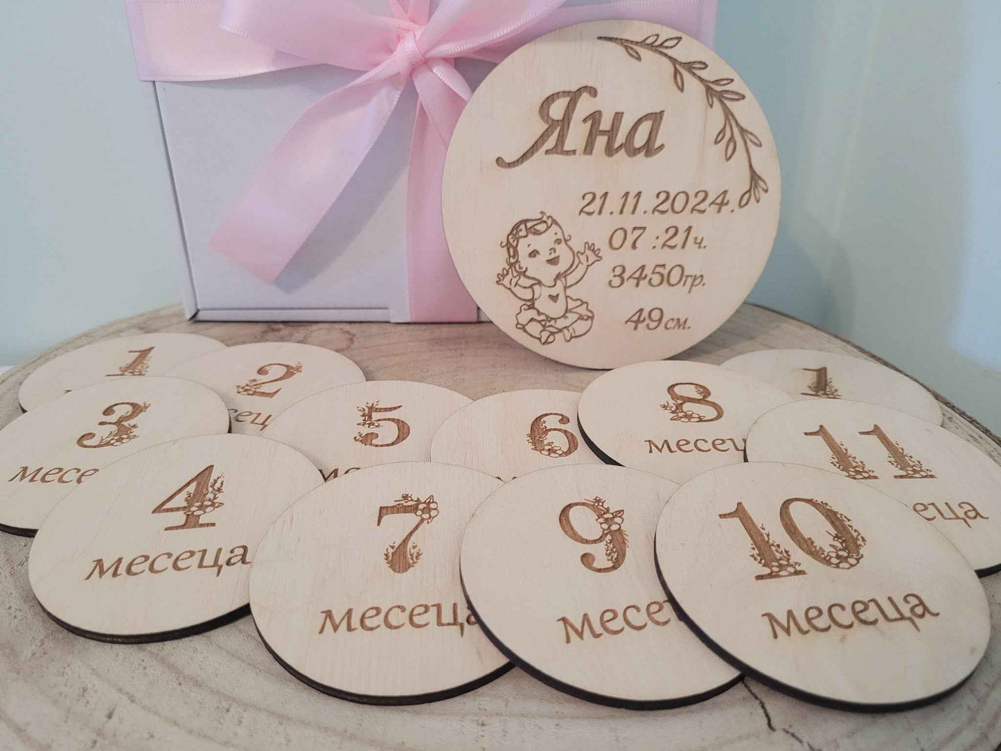 Wooden milestone discs with numbers and text, placed on a surface with a gift box in the background.