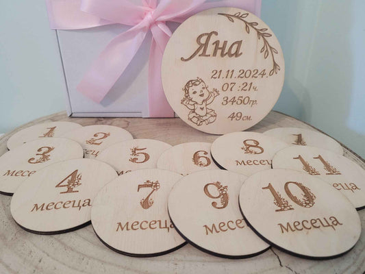 Wooden milestone discs with numbers and text, placed on a surface with a gift box in the background.