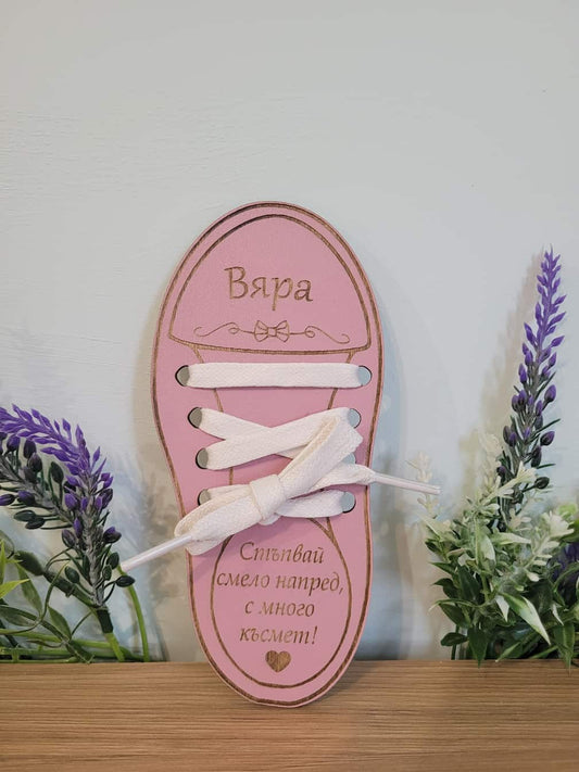 Pink shoe-shaped decorative item with white laces on a wooden surface with plants in the background