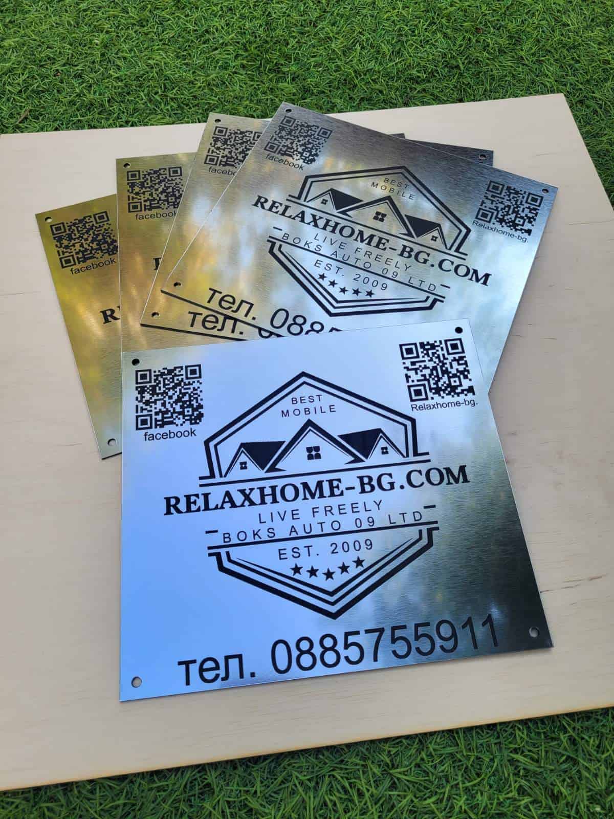 Metallic business signs with QR codes and text on a wooden surface.