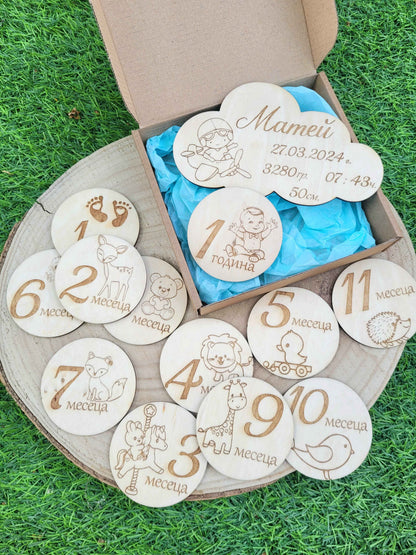 Wooden milestone discs with baby illustrations and numbers in a box on grass