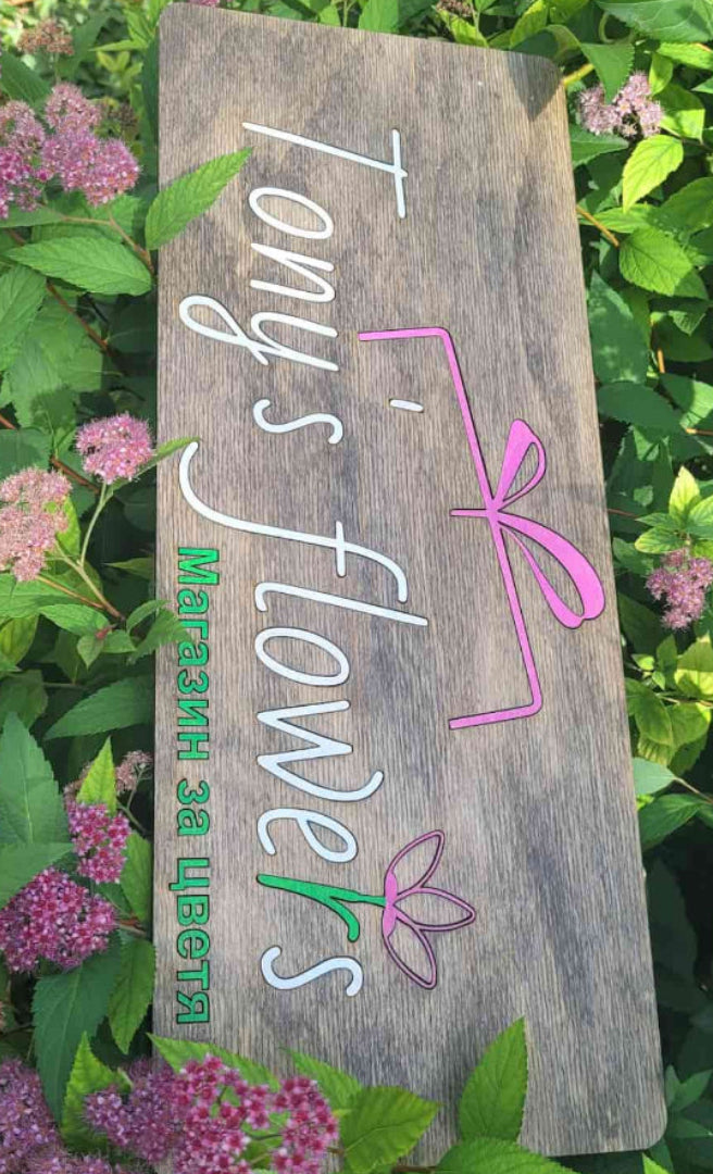 Wooden sign with 'Tony's flowers' branding surrounded by greenery and flowers