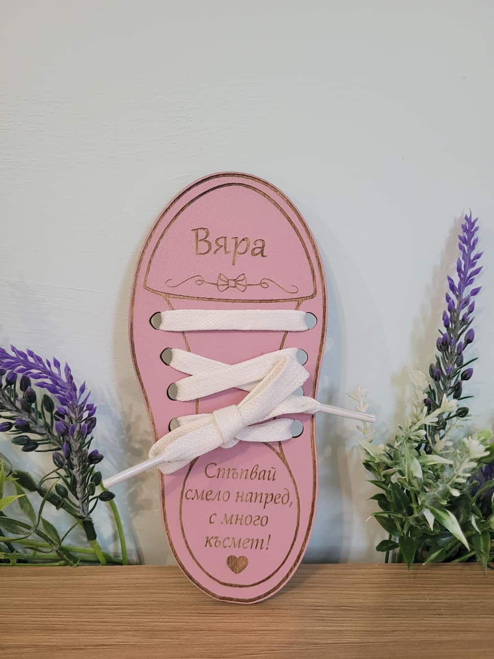 Pink shoe-shaped decorative item with white laces on a wooden surface with plants in the background