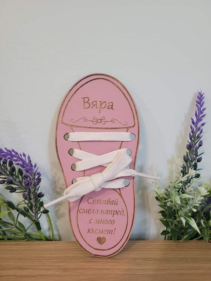 Pink shoe-shaped decorative item with white laces on a wooden surface with plants in the background